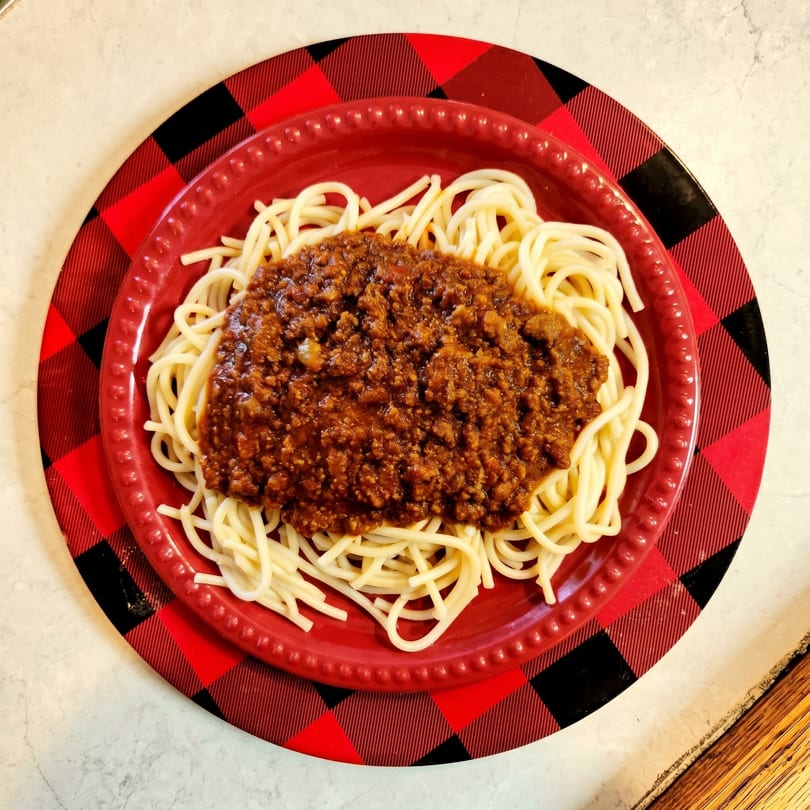 Spaghetti with meat sauce on a red plate, atop a red and black plaid placemat.
