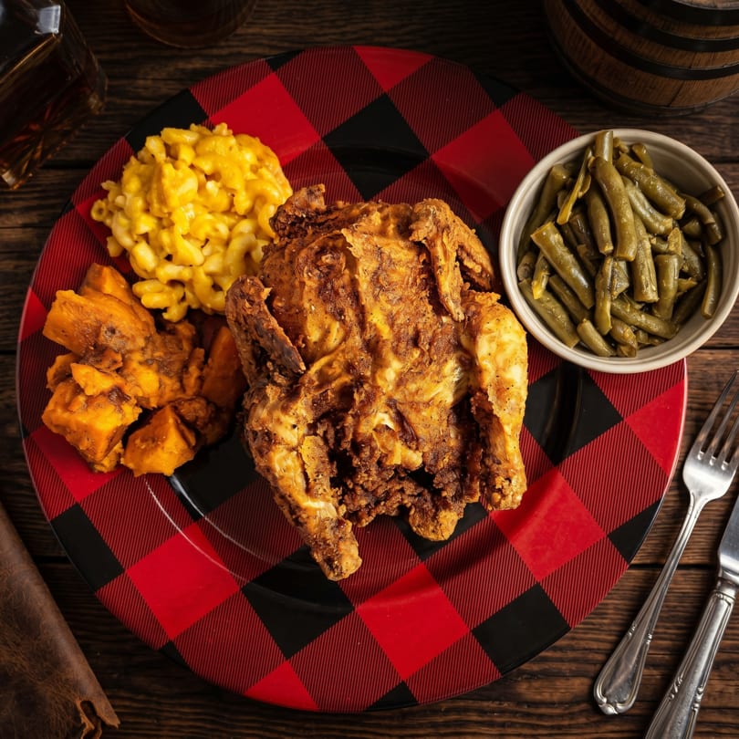 Fried chicken, macaroni and cheese, sweet potatoes, and green beans on a red and black plaid plate.