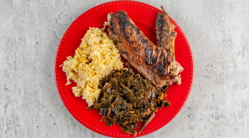 Grilled turkey wing, yellow rice, and collard greens on a bright red plate.